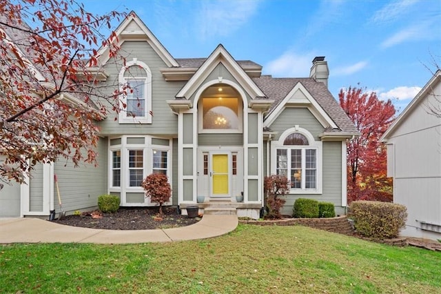 traditional home with a front yard, roof with shingles, and a chimney