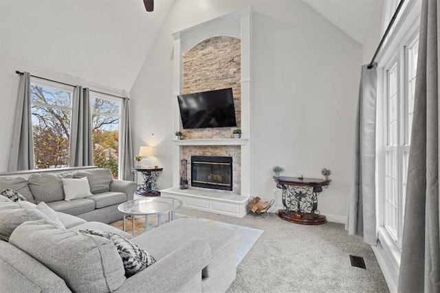 carpeted living area with high vaulted ceiling, visible vents, a stone fireplace, and baseboards