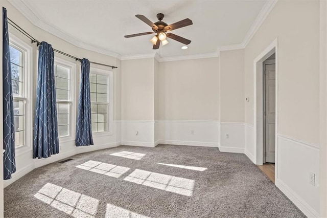 carpeted spare room with baseboards, visible vents, ornamental molding, and a ceiling fan