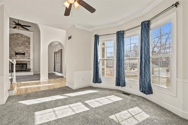 unfurnished room featuring baseboards, visible vents, arched walkways, ornamental molding, and a stone fireplace