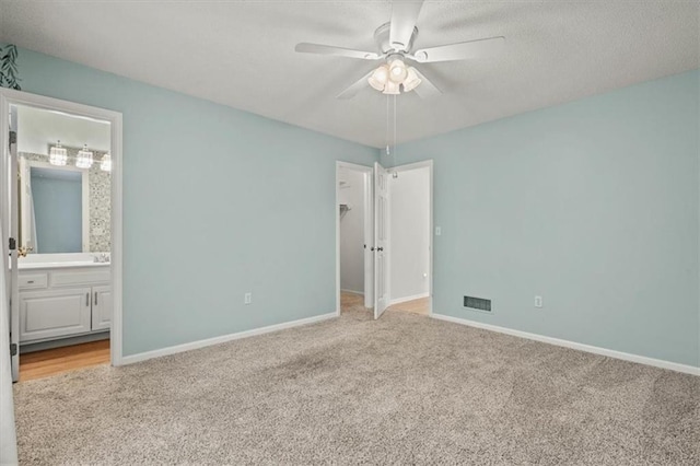 unfurnished bedroom featuring light carpet, a walk in closet, visible vents, and baseboards