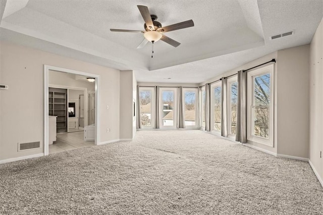 carpeted spare room featuring visible vents, a tray ceiling, and a textured ceiling