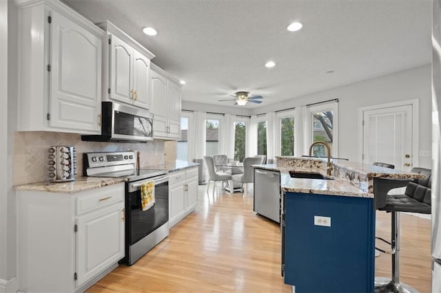 kitchen with light wood finished floors, a breakfast bar area, stainless steel appliances, white cabinetry, and a sink