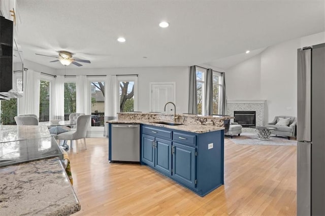 kitchen featuring a tiled fireplace, appliances with stainless steel finishes, open floor plan, blue cabinetry, and a sink