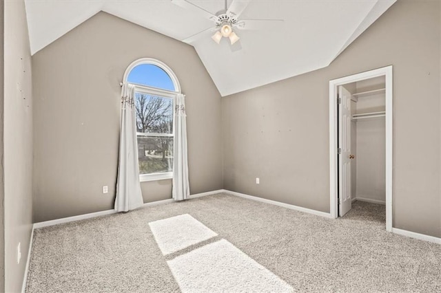 unfurnished bedroom with carpet floors, a ceiling fan, baseboards, vaulted ceiling, and a walk in closet