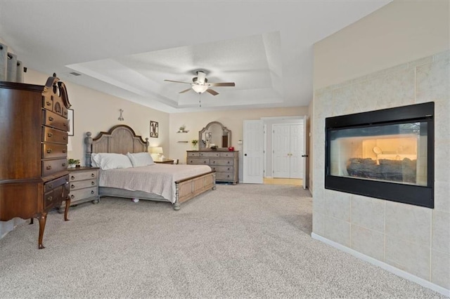 carpeted bedroom featuring ceiling fan, a tray ceiling, a tile fireplace, and baseboards