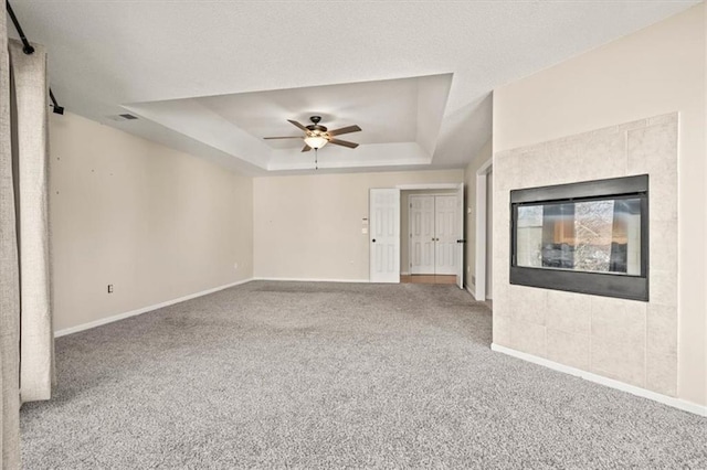 unfurnished living room featuring carpet floors, a fireplace, baseboards, and a raised ceiling