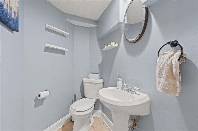 half bathroom with baseboards, toilet, and tile patterned floors