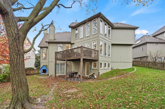 rear view of property featuring a wooden deck, a chimney, fence, and a lawn