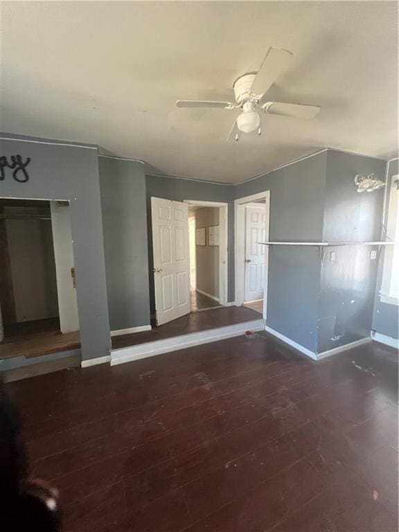 unfurnished room featuring baseboards, dark wood finished floors, and a ceiling fan