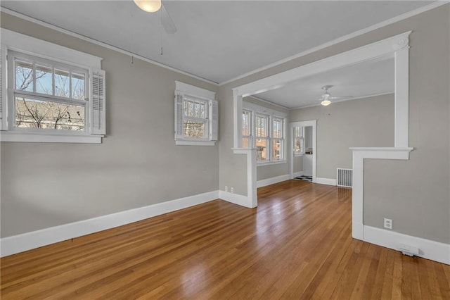 empty room with visible vents, baseboards, ornamental molding, a ceiling fan, and hardwood / wood-style floors