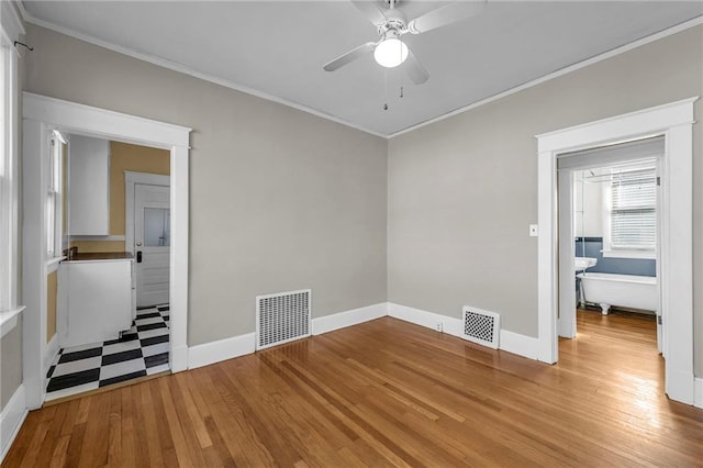 empty room with ceiling fan, wood finished floors, visible vents, and crown molding