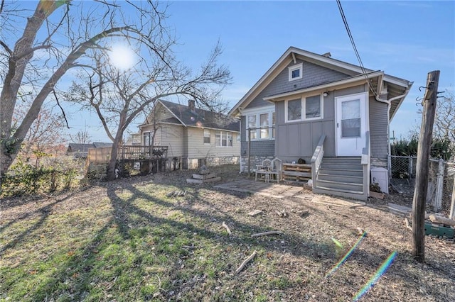 rear view of house with board and batten siding, entry steps, and fence