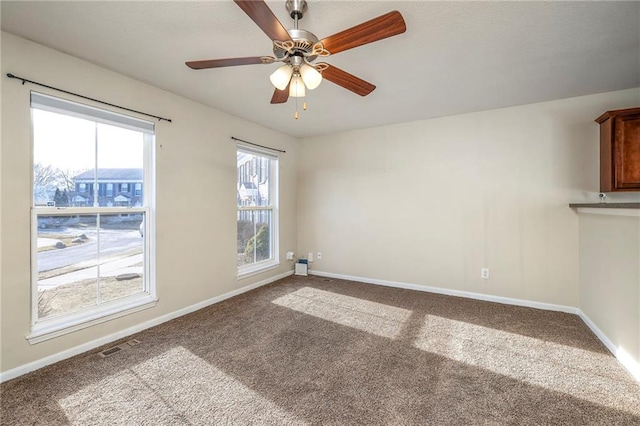 carpeted spare room with a ceiling fan, visible vents, and baseboards