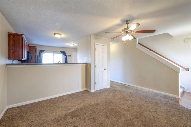 unfurnished living room featuring carpet floors, a ceiling fan, a textured ceiling, baseboards, and stairs