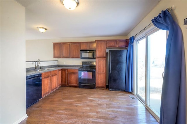 kitchen with visible vents, brown cabinetry, light wood-style floors, black appliances, and a sink