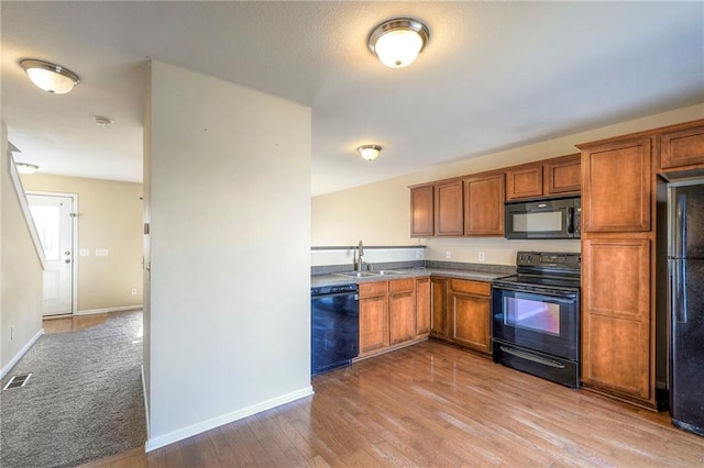 kitchen featuring brown cabinetry, a sink, black appliances, wood finished floors, and baseboards