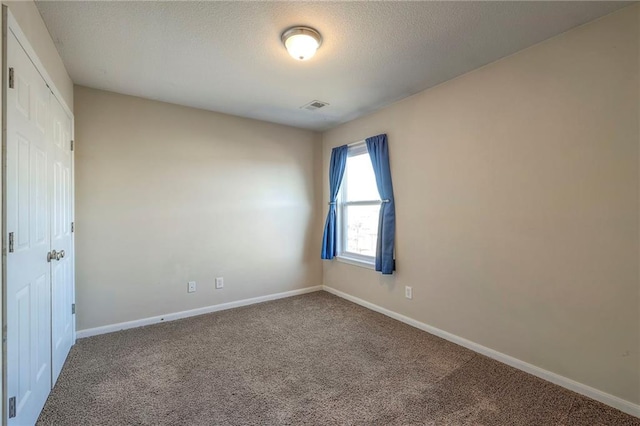 empty room featuring a textured ceiling, carpet floors, visible vents, and baseboards