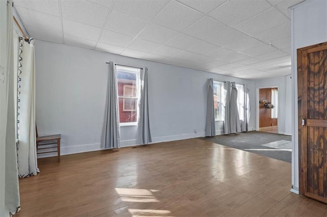 unfurnished room featuring a paneled ceiling, plenty of natural light, baseboards, and wood finished floors