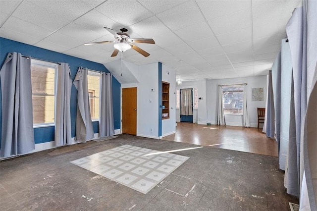 interior space featuring a drop ceiling, a ceiling fan, and baseboards