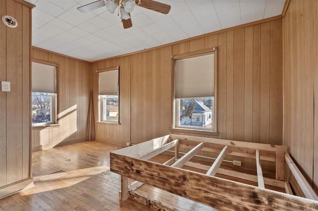 interior space with a ceiling fan, wood-type flooring, plenty of natural light, and wood walls