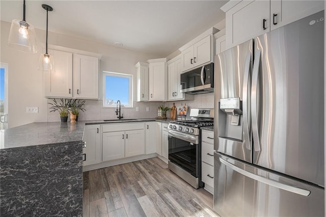 kitchen featuring stainless steel appliances, decorative backsplash, white cabinets, a sink, and light wood-type flooring