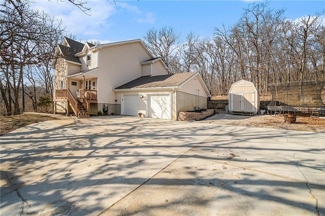 view of side of property with a shed, stairway, concrete driveway, an outbuilding, and an attached garage