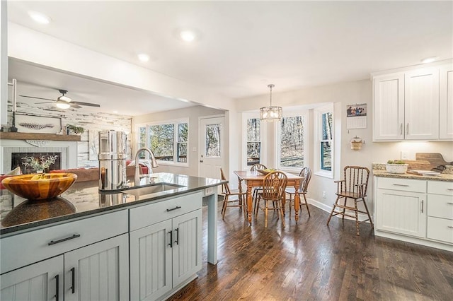 kitchen with dark wood-type flooring, a sink, decorative light fixtures, dark stone countertops, and a fireplace