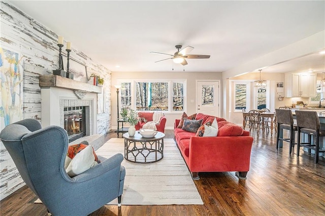 living area featuring a wealth of natural light, a glass covered fireplace, dark wood finished floors, and a ceiling fan