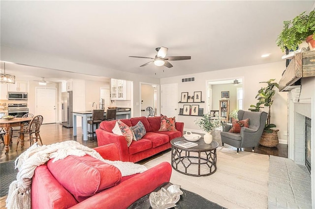 living room featuring visible vents, wood finished floors, a fireplace, and a ceiling fan