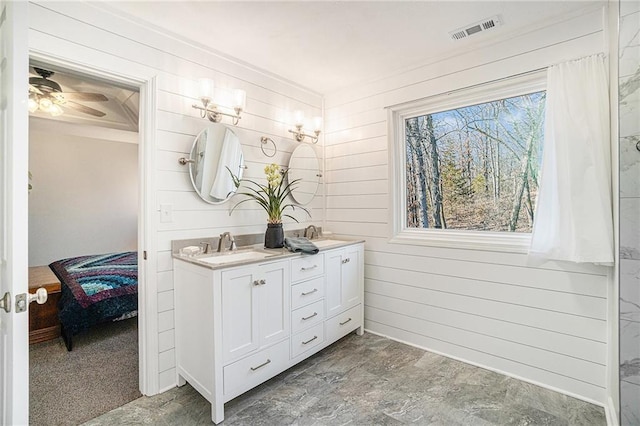 ensuite bathroom featuring visible vents, a sink, connected bathroom, wood walls, and double vanity