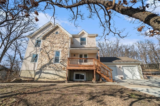 back of property with stone siding, stairway, concrete driveway, an attached garage, and a wooden deck