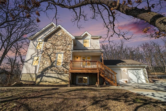 back of house at dusk with stone siding, driveway, an attached garage, and stairs