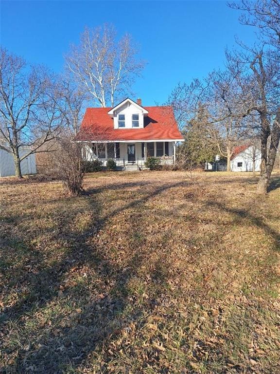 view of front of house featuring covered porch, a chimney, and a front yard