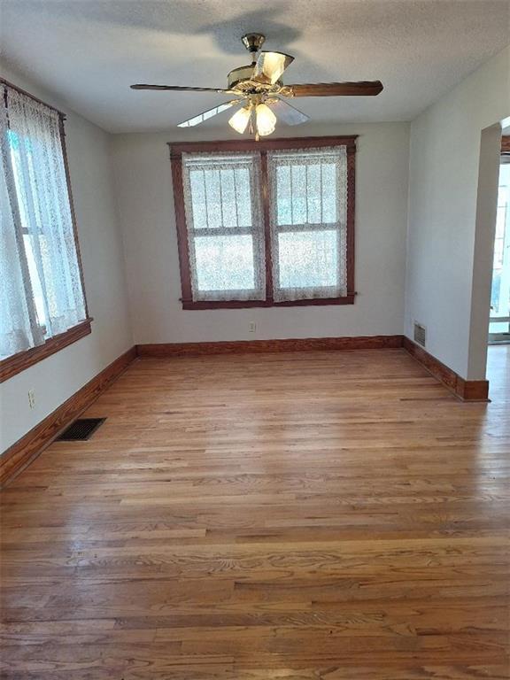 empty room with visible vents, a textured ceiling, baseboards, and wood finished floors