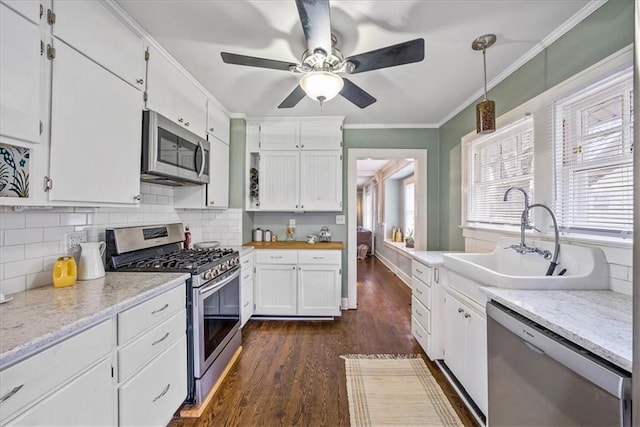 kitchen featuring stainless steel appliances, a sink, white cabinetry, decorative light fixtures, and crown molding