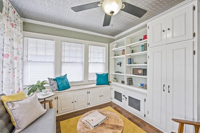 living area featuring a ceiling fan, an ornate ceiling, ornamental molding, and dark wood-style flooring