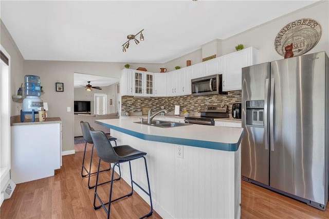 kitchen with stainless steel appliances, tasteful backsplash, light wood-style floors, glass insert cabinets, and a sink