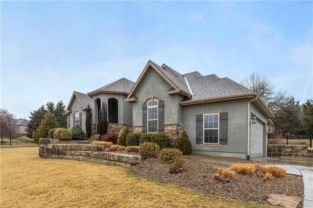 view of front of home with a shingled roof, stone siding, an attached garage, a front lawn, and stucco siding