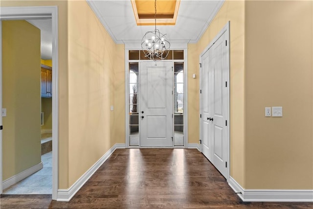 foyer entrance with a tray ceiling, a notable chandelier, crown molding, wood finished floors, and baseboards