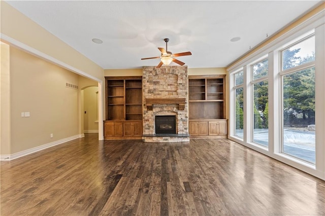 unfurnished living room with arched walkways, a fireplace, baseboards, and wood finished floors