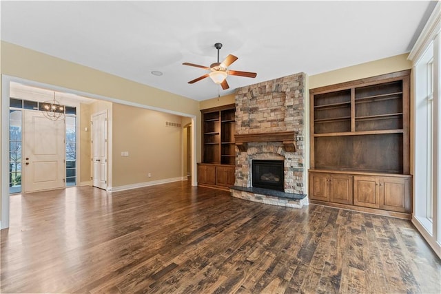 unfurnished living room featuring built in features, a fireplace, wood finished floors, baseboards, and ceiling fan with notable chandelier