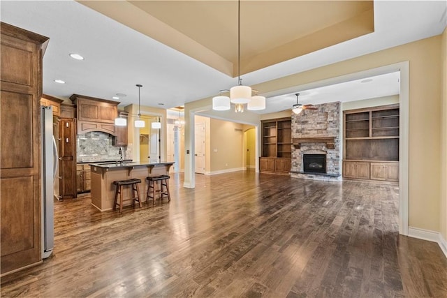 living area with dark wood-style floors, baseboards, a fireplace, and a tray ceiling