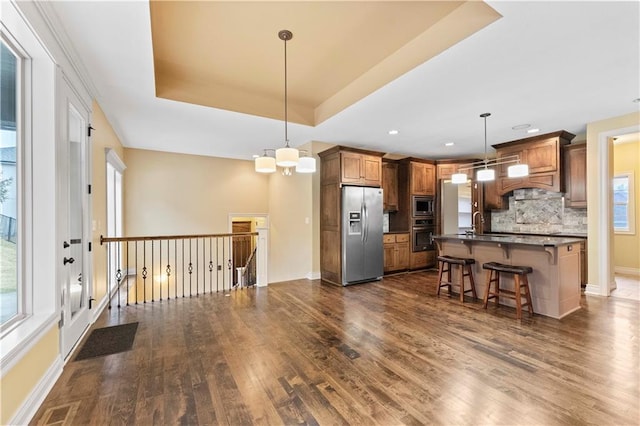 kitchen featuring dark wood-style floors, a tray ceiling, a breakfast bar area, stainless steel appliances, and dark countertops