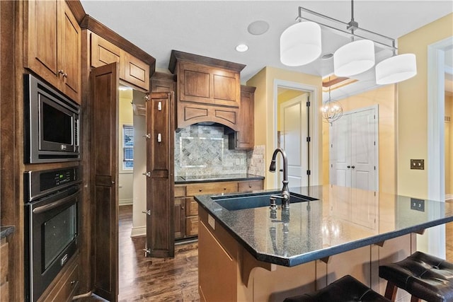 kitchen featuring dark wood finished floors, stainless steel microwave, decorative backsplash, a sink, and oven