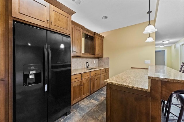 kitchen featuring a sink, a kitchen breakfast bar, black fridge, decorative backsplash, and brown cabinets