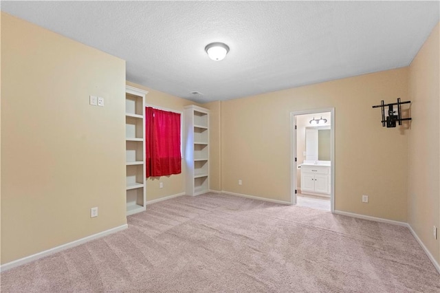 unfurnished bedroom with light carpet, a textured ceiling, baseboards, and ensuite bathroom