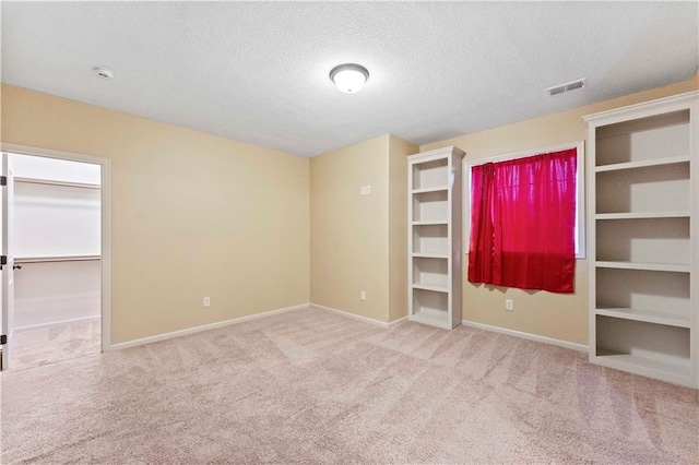 unfurnished bedroom featuring a textured ceiling, carpet floors, visible vents, baseboards, and a spacious closet