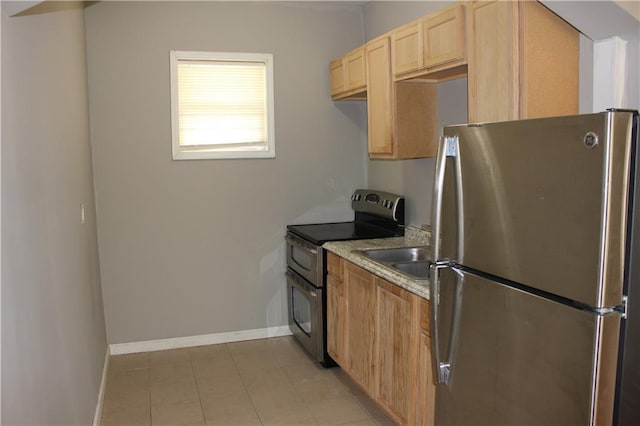 kitchen with stainless steel appliances, light countertops, light brown cabinets, a sink, and baseboards