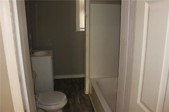 bathroom featuring a bath, vanity, toilet, and baseboards